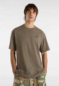 Olive green cotton t-shirt with a crew neckline, short sleeves, and a small logo detail on the chest, paired with camo-patterned shorts.