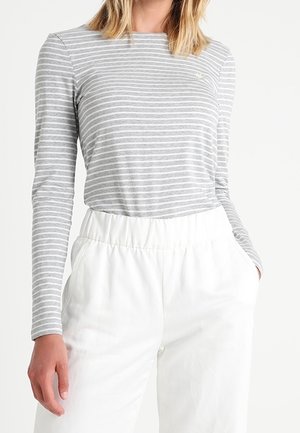 Femme portant un haut ajusté à manches longues rayé gris et blanc, rentré dans un pantalon blanc ample taille haute avec des poches.