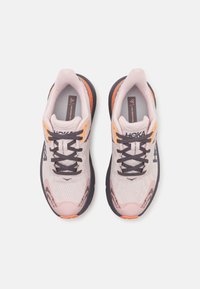 Scarpe da corsa rosa chiaro con suole nere, accenti arancioni, tomaia in rete e lacci rotondi. Presenta il logo di lato e un design testurizzato.