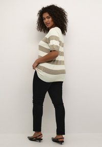 Sweter w paski w kolorze kremowym i taupe, krótki rękaw, luźny krój, zestawiony z czarnymi wąskimi dżinsami i czarnymi sandałami na obcasie.