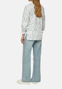 Witte trui met een gespikkeld patroon, lange mouwen en zijsplitten, gecombineerd met lichtblauwe wijde jeans en witte sneakers.