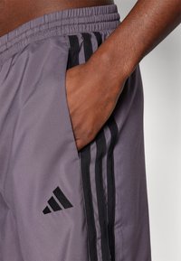 Grey athletic shorts with a smooth texture, featuring black side stripes, an elastic waistband, and an Adidas logo on the left side.