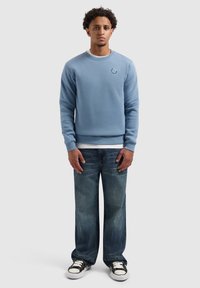 Lichtblauwe sweatshirt van katoen, met een ronde hals en geribde mouwen. Gekoppeld aan losse, vervaagde jeans en zwarte sneakers.
