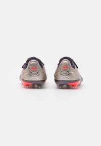 Voetbalschoenen met een zilveren synthetisch bovenwerk, paarse accenten en een rode hiel. Uitrusting met een gestructureerde grip en een laag profiel ontwerp.