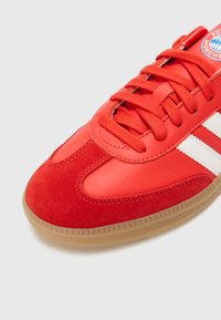Röd sportskotek som har en kombination av slät läder och texturerad mocka, med vita ränder och en sål av gummigummi.