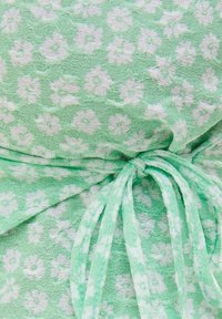 Tessuto verde chiaro a motivo floreale con piccoli motivi bianchi, dotato di un dettaglio annodato in vita con fiocco coordinato. Materiale morbido e texture.