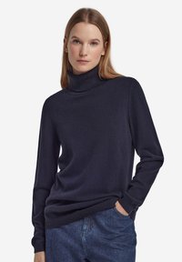 Marinblå polotröja i mjukt tyg, långärmad med ribbade ärmslut och fåll, kombinerad med blå denimjeans. Inga synliga mönster eller detaljer.