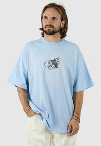 Tricou oversized din bumbac de culoare albastru deschis, cu mâneci scurte și un grafic în negru și gri în centru. Croială casual și guler ribarit.