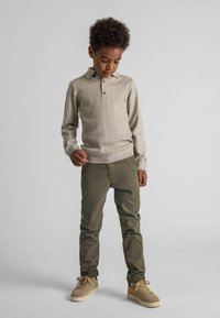 Beige gebreide trui met een gestructureerd patroon, henley-kraag, knoopdetail, gecombineerd met olijfgroene slim-fit broek en beige sneakers.