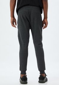 Grå sweatpants lavet af et blødt, struktureret stof, med elastisk talje og ribbede manchetter, samt synlige sømdetaljer på benene.