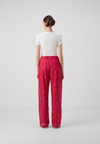 Rosa spetsbyxor med lös passform, utsmyckade med blommönster och hög midja. Bärs med en åtsittande vit t-shirt, sedd från baksidan.