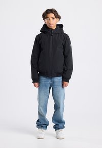 Black zip-up jacket with a hood, ribbed cuffs, and two front pockets, paired with light blue jeans and white sneakers.