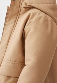 Giacca puffer beige con una texture liscia. Caratterizzata da un cappuccio e da una grande tasca frontale, con un dettaglio di cucitura lungo le maniche.