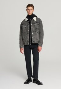Giacca di denim grigia con colletto in shearling bianco, due tasche sul petto e chiusura a bottoni, abbinata a pantaloni neri e scarpe.