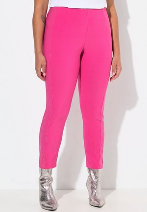 Pantalons roses ajustés avec une texture lisse et des détails sur les côtés, associés à des bottines argentées brillantes.