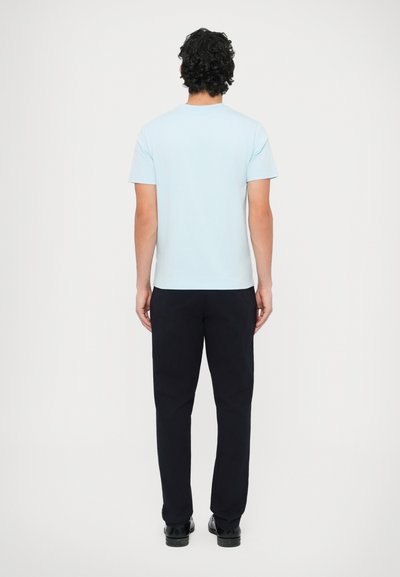 Ανοιχτό γαλάζιο κοντομάνικο μπλουζάκι, από βαμβακερό υλικό, με άνετη εφαρμογή. Φορεμένο με σκούρο μπλε παντελόνι και μαύρα παπούτσια, λιτός σχεδιασμός, χωρίς σχέδια.