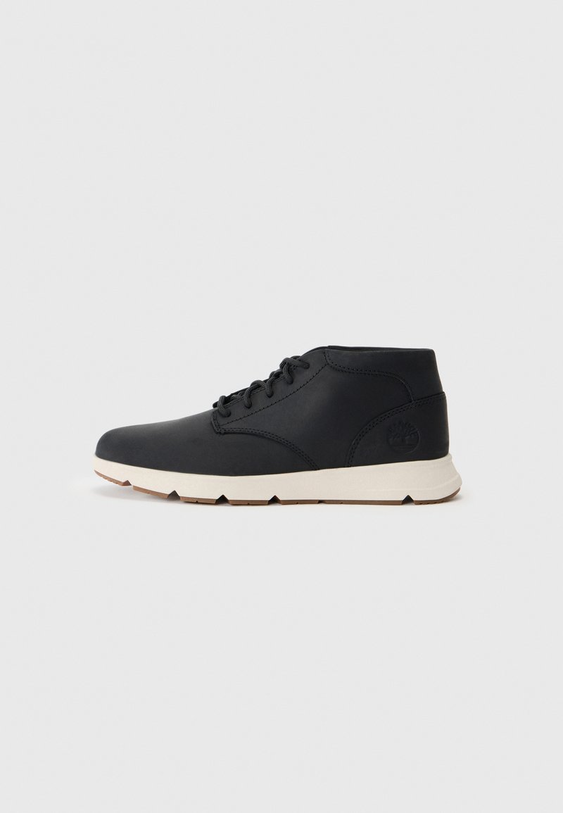 Botas chukka de cuero negro con una suela de goma blanca, que cuentan con cordones redondos y un logo en relieve en el talón. Textura suave en toda la superficie.