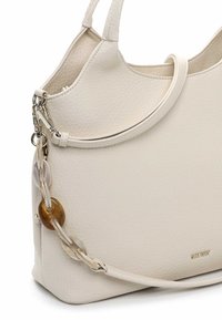 Kermaankermanvärinen nahkalaukku, jossa on tekstuuri, pyöreä kahva ja koristeellinen linkkiketju.