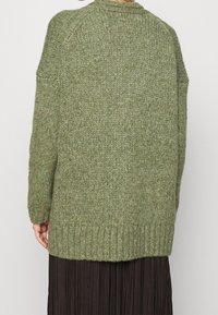 Green knitted sweater, oversized design, ribbed hem, soft texture, and raglan sleeves. The back features a simple, seamless finish.