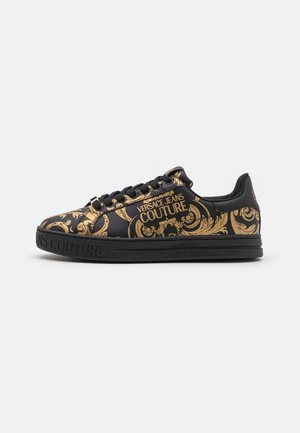 Czarny niski sneaker ze złotymi barokowymi wzorami i tekstem "Versace Jeans Couture" na boku i podeszwie, pokazany w prawym profilu.