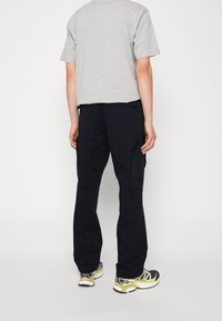 Camiseta de hombre de manga corta en color gris combinada con pantalones cargo negros que tienen bolsillos laterales, corte recto y zapatillas negras y amarillas.
