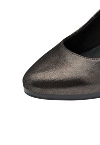 Ingrandimento di una scarpa flat da donna con texture metallica, punta arrotondata e suola nera su sfondo bianco.