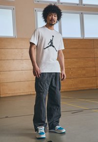 Hvid t-shirt med sort grafik, grå cargo-bukser og blå sneakers. Casual sportstøj, der viser komfort og funktionalitet.