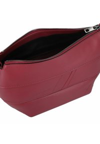 Borsa a mano in pelle rossa con una superficie liscia, chiusura con zip e design angolare. L'interno è nero e presenta dettagli hardware minimali.