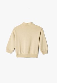 Suéter beige con un alto cuello, hombros caídos y puños acanalados. Tejido suave con una textura lisa, que se extiende hasta un dobladillo corto.