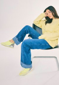 Yellow sneakers with black and white zebra print accents, worn with rolled-up blue denim jeans and a loose-fitting yellow sweater.
