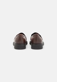 Chaussures en cuir marron avec une finition lisse, bout arrondi et semelles en caoutchouc noires. Design minimaliste sans motifs ou éléments visibles.