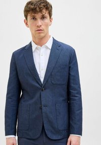 Blazer en lin navy avec deux poches avant et une fermeture à un bouton, porté sur une chemise blanche à col. Texture lisse, coupe ajustée.