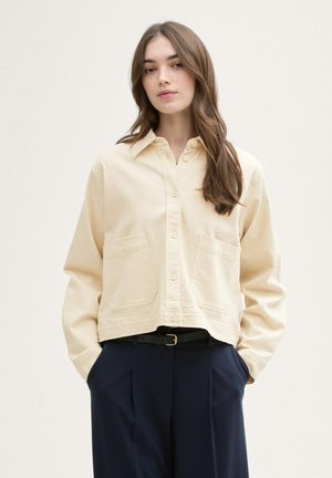 Beige overhemd met knopen, een puntkraag, twee voorzakken, een cropped ontwerp en lange mouwen, gecombineerd met marineblauwe broeken.