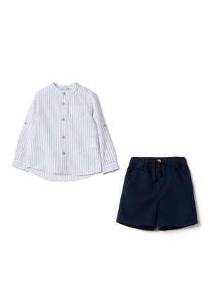 Weißes Langarmhemd mit Streifen und Holzknöpfen, kombiniert mit marineblauen Shorts mit elastischem Bund.