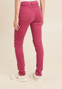 Fitte roze denim jeans met een gladde textuur, een middelhoge taille en twee achterzakken. Gepaarde met witte sneakers met beige accenten.