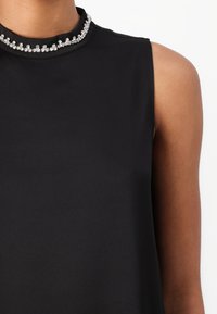 Black sleeveless top featuring a smooth texture, high neck, and a decorative silver jeweled collar. No visible patterns or accents on the fabric.