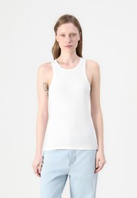 Hvit ribbestrikket tanktop med rund hals og brede stropper, tettsittende fasong og myk bomullstekstur.
