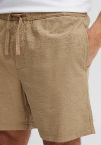 Beige shorts met een gestructureerde stof, een tailleband met trekkoord en zijzakken, voorzien van een subtiele patroonafwerking en een rechte zoom.