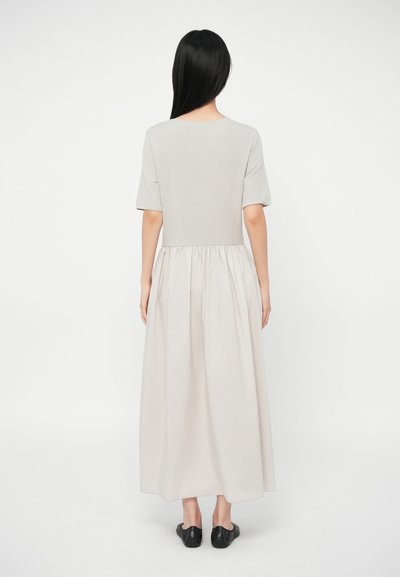 Ilga, šviesiai pilka suknelė su prigludusia liemenėle, trumpomis rankovėmis ir surinkta sijonu. Lygus audinio paviršius ir apvalus iškirpimas. Lygūs juodi batai.