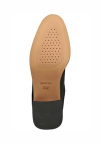 Suola di scarpa nera con una base liscia di colore marrone chiaro, caratterizzata da piccole perforazioni per la traspirabilità e un motivo testurizzato per migliorare la presa.