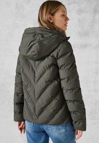 Giacca a vento imbottita di colore verde scuro, dotata di cappuccio, trapuntatura a chevron e una vestibilità comoda. Realizzata in materiale trapuntato e leggero.