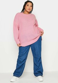 Rosa stickad tröja med långa ärmar, lös passform och ribbat mönster. Kombinerad med blå vida jeans och vita sneakers.