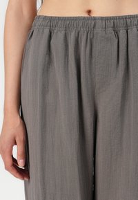 Pantalons tissés légers et gris, dotés d'une taille élastique, d'une coupe ample et d'une texture subtile, avec un détail de poche latérale visible.