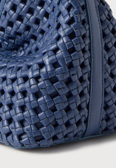 Κοντινή λήψη γωνίας υφασμένης τσάντας από ναυτικό μπλε δέρμα με λεία δερμάτινη λεπτομέρεια σε λευκό φόντο.