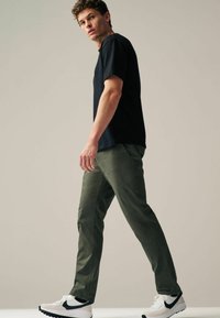 Dark navy t-shirt, olive green pants, and white sneakers with black accents. The outfit features a relaxed fit and soft textures.
