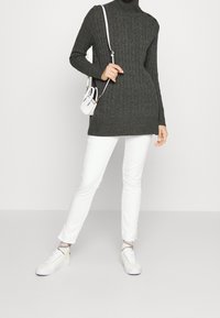Šedý, ribovaný rolák s detalními knoflíky, kombinovaný s bílými slim-fit kalhotami a bílými teniskami. Malá bílá přes rameno taška.