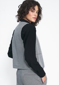 Szary kamizelka w zygzaki na czarnej koszuli z długim rękawem, charakteryzująca się dopasowanym krojem i teksturą w jodełkę, z bocznymi kieszeniami i prostymi liniami.