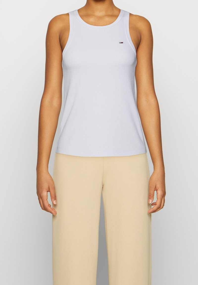 Top in un delicato viola con un design aderente, scollatura rotonda e spalline sottili. Presenta un piccolo logo sul petto. Abbinato con pantaloni beige.
