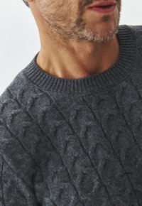 Harmaa neulottu villapaita, jossa on kaapelikuvio, ribbireunuksellinen pyöreä pääntie ja pehmeä texture. Lähikuva korostaa neulontayksityiskohtia.