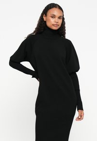 Μαύρο, ριγέ πλεκτό φόρεμα με ψηλό λαιμό, φουσκωτά κοντά μανίκια και λεπτή ριγέ κάτω περιοχή.